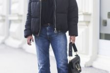 an edgy look with a black top, blue straight jeans, black boots, an oversized black puffer jacket and a black bag