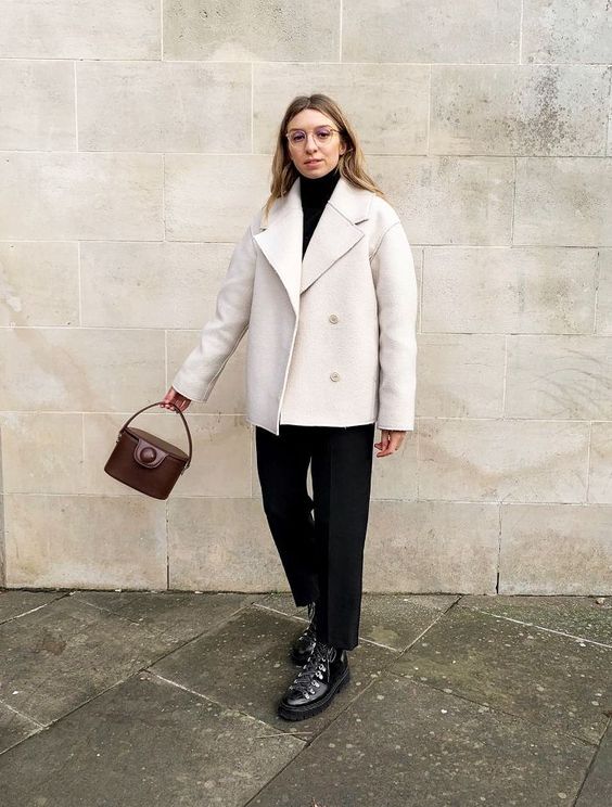 a monochromatic look with a black turtleneck, black trousers, black hiking boots, a white coat and a brown bucket bag