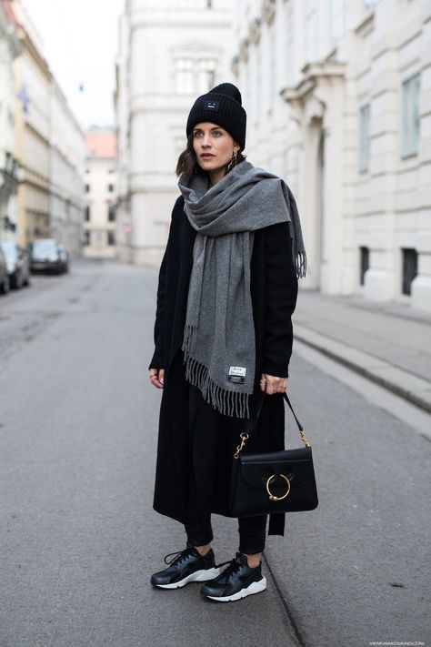 a total black look with skinnies, a midi coat, a beanie, trainers, a bag and a large grey scarf