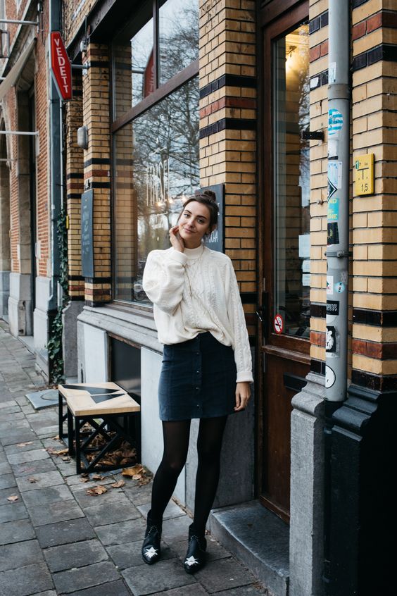 a white oversized sweater, a dark green denim mini with buttons, black tights and booties