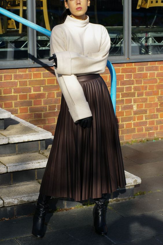 an edgy look with an oversized white sweater, a brown leather midi skirt and black boots