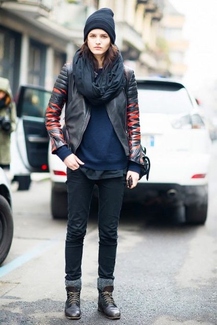 With navy blue sweater, black pants, black and red leather jacket, hat and gray socks