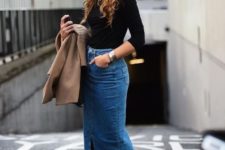 a chic look with a black turtleneck, a blue denim midi skirt with a slit, blakc shoes and a tan coat