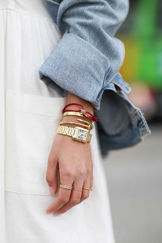 a combo of two gold bracelets, a dainty chain bracelet, a watch and a red bracelet with a seashell for an edgy look