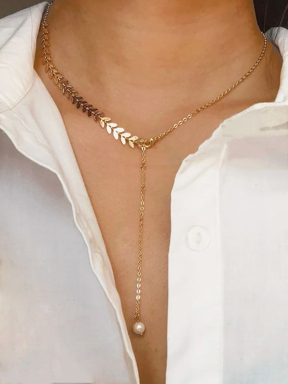 a gold lariat necklace with a chain and a leafy part and a pearl on its end for an even trendier look