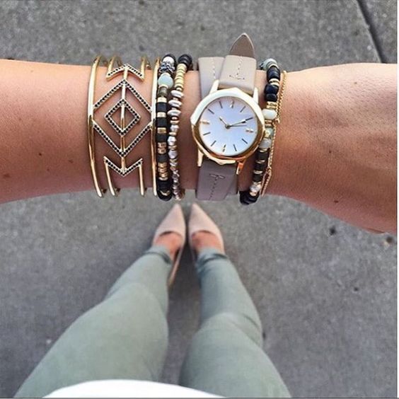 a stack of bracelets with beads, a statement geometric one and a watch on a grey leather strap