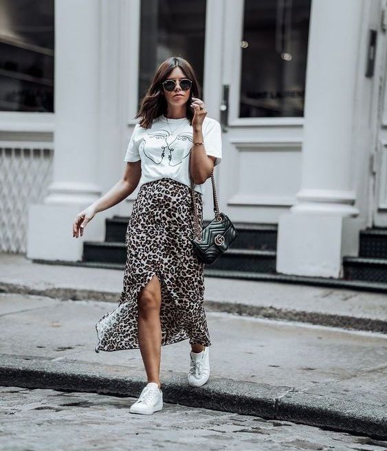 a white printed tee, a leopard print midi skirt with a front slit, white sneakers and a black bag on chain