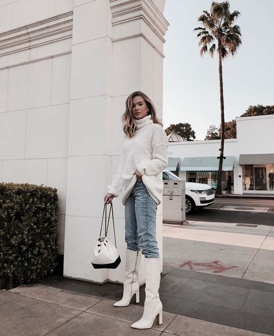 an oversized white sweater, light blue jeans, white knee boots and a black and white backpack
