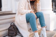 blue skinnies with a raw hem, white heeled booties, a white faux fur midi coat and a brown backpack