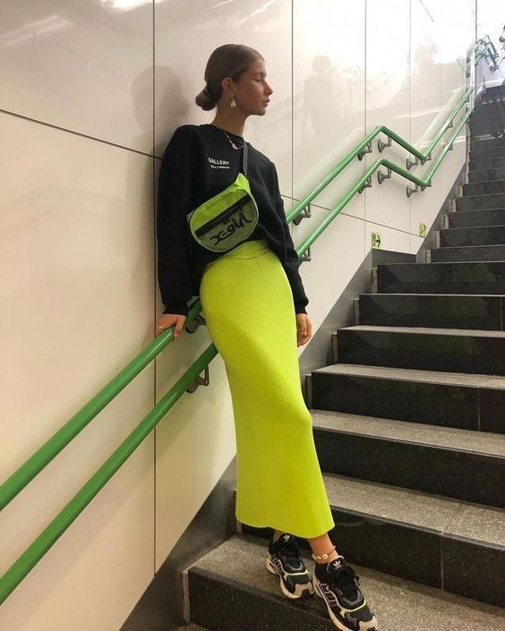 a trendy sporty look with a black sweatshirt, a neon yellow skirt, black and white trainers and a neon green bag