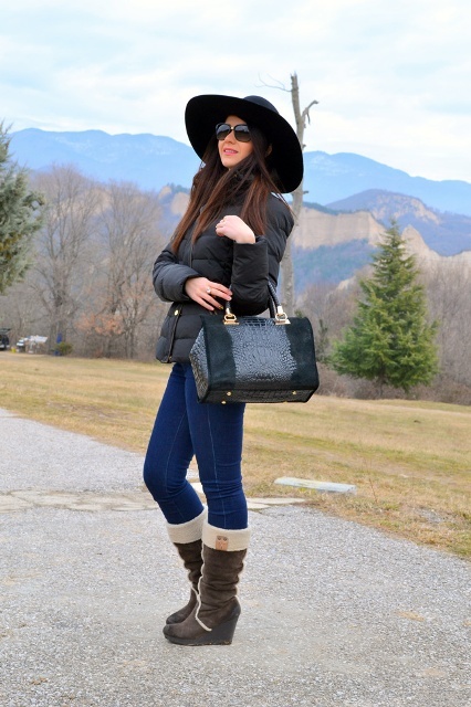 With black wide brim hat, black puffer jacket, leather and suede bag and jeans