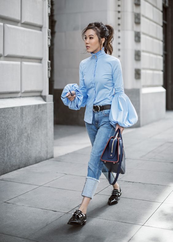 a daring look with a blue puffy sleeve blouse in Victorian style, blue jeans, black shoes and a navy bag