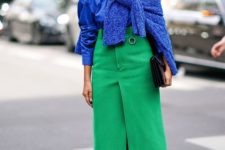 a trendy colorful outfit with a classic blue shirt, sweater, a bold green midi skirt, white shoes and a clutch
