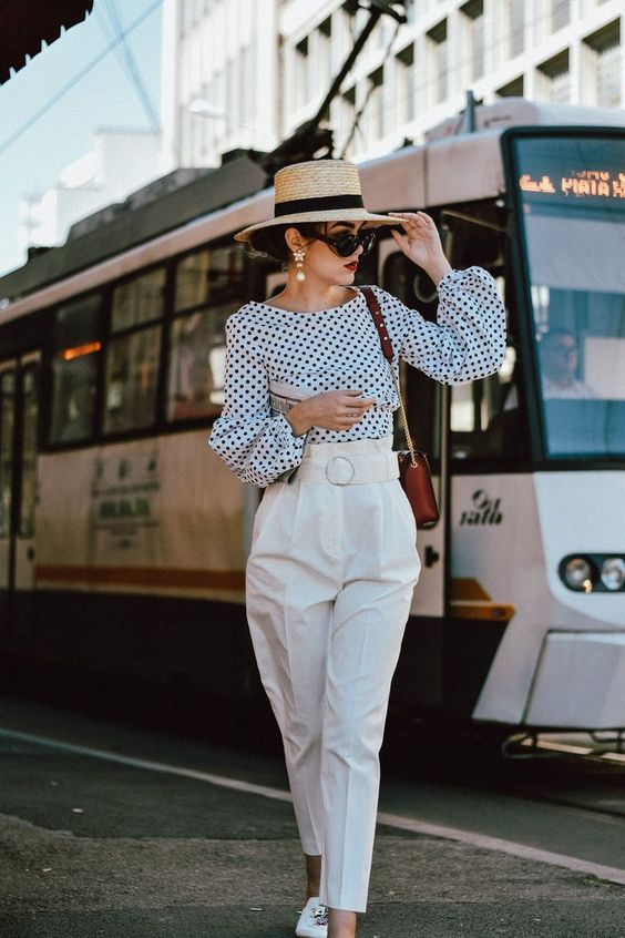 a vacation look with white trousers, a polka dot puffy sleeve blouse, a hat and statement earrings