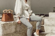 a vacation outfit with a white puffy sleeve blouse on buttons, checked pants, white sneakers and a brown bag