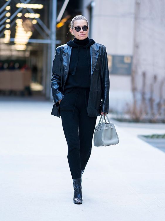 Yolanda Hadid wearing a black hoodie, black pants, booties, a black lacquer leather blazer and carrying a blue bag