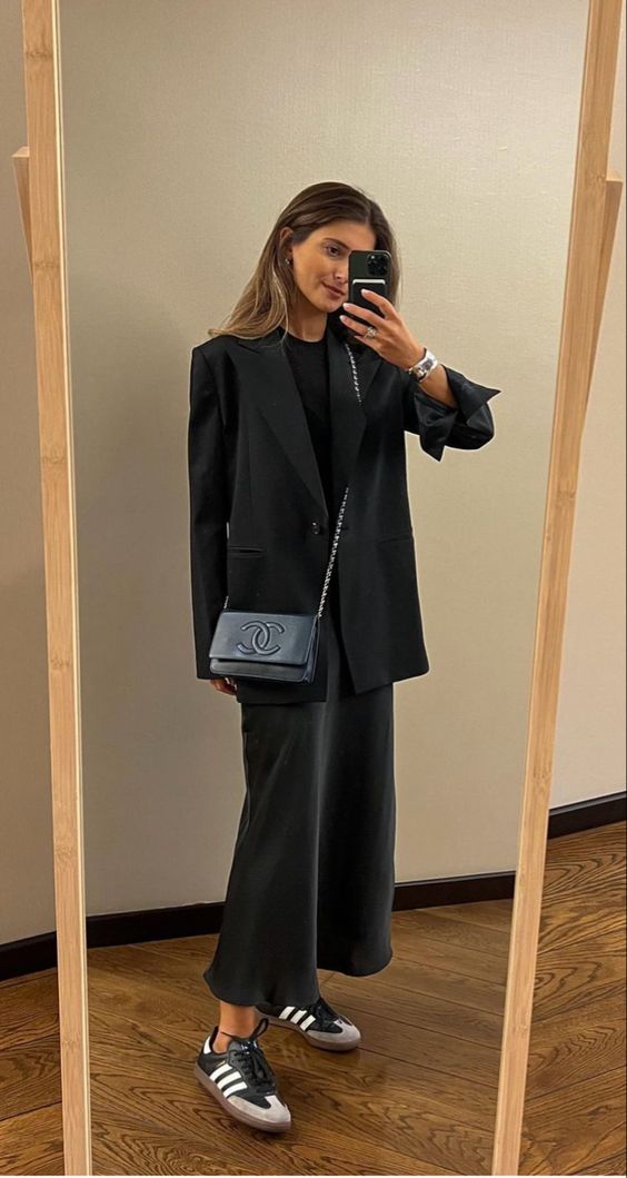 a black outfit with a t-shirt, a satin maxi skirt, an oversized blazer, a bag and striped sneakers