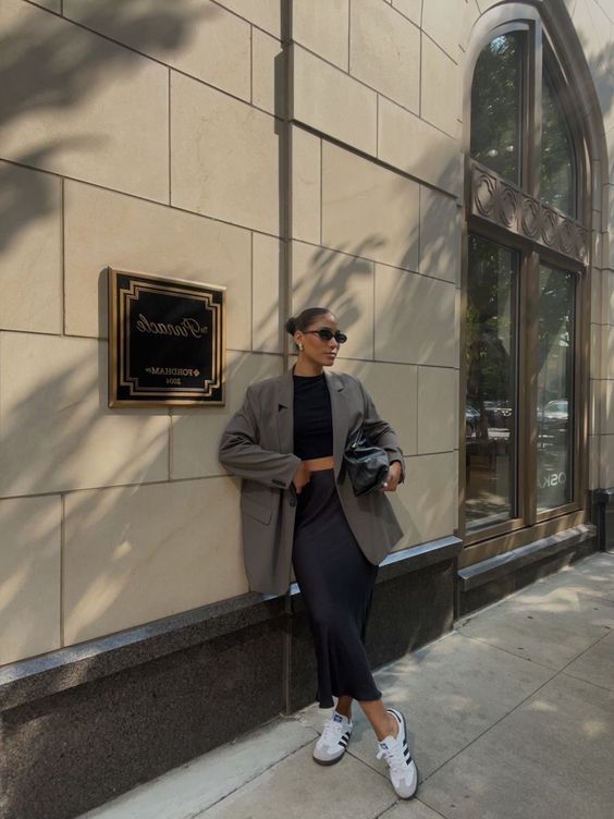 a chic spring outfit with a black crop top, a black satin midi skirt, a grey oversized blazer and white sneakers, a large black bag