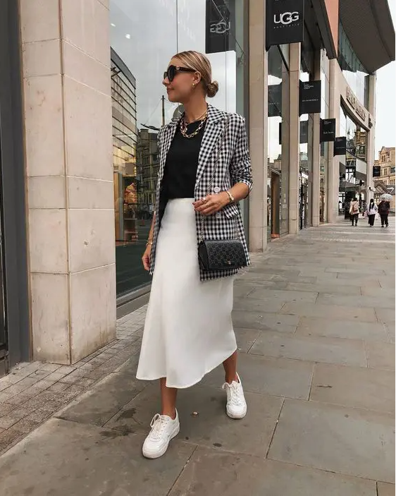A monochromatic work look with a black t shirt, a white slip midi skirt, white sneakers, a printed black and white blazer and a black bag