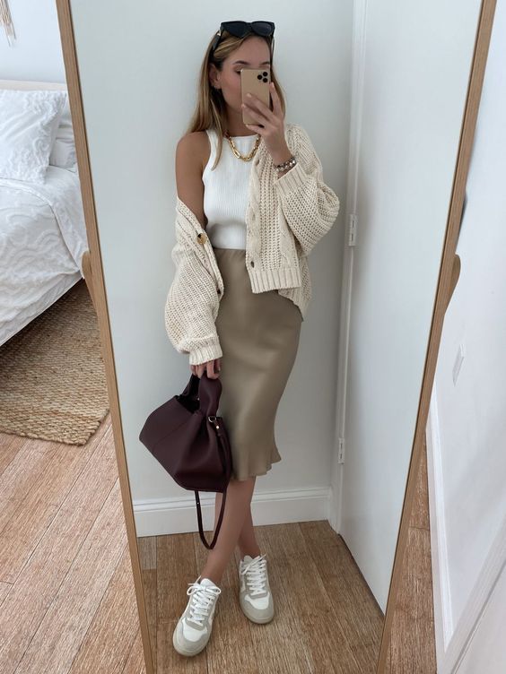 a neutral spring look with a white tank top, a tan satin midi skirt, a neutral cardigan, neutral sneakers and a burgundy bag