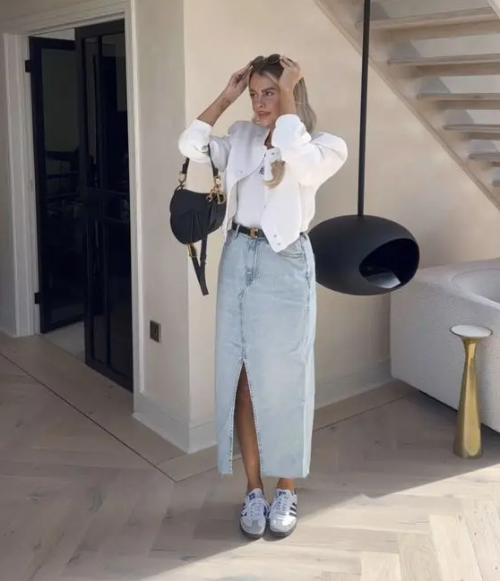 a white top, a bleached denim maxi, trainers, a white cropped bomber jacket, a black saddle bag and belt
