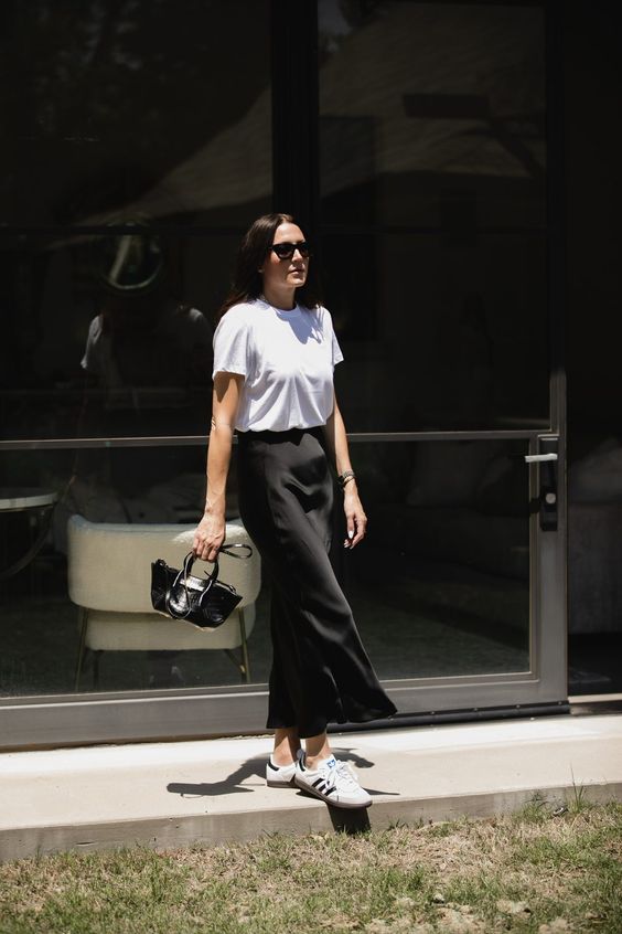An easy summer look with a white t shirt, a black satin midi skirt, neutral sneakers, a small and chic black bag