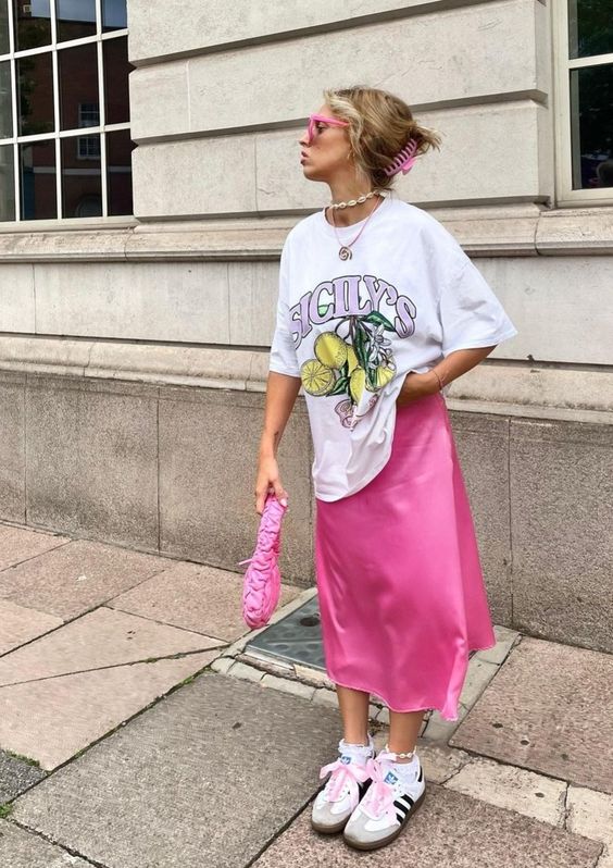 A bright spring look with a printed t shirt, a hot pink satin midi skirt, white sneakers, layered necklaces, a pink bag and sunglasses