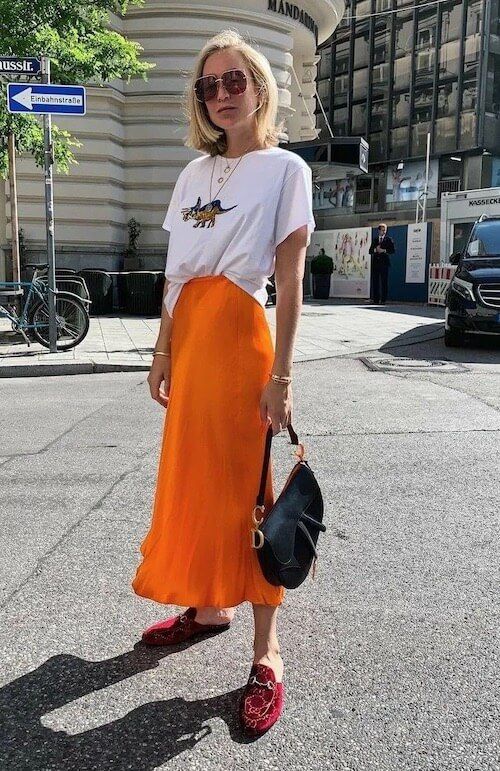 a bright spring look with a printed tee, a marigold satin midi skirt, red slipper mules, a black saddle bag