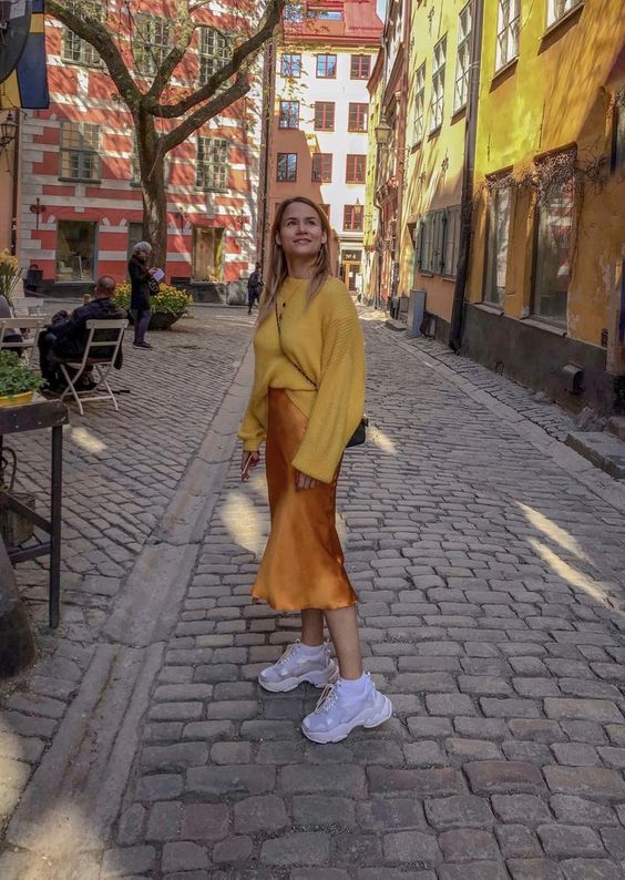 a bright spring look with a yellow oversized jumper, a marigold satin midi skirt, white trainers and socks for colder days