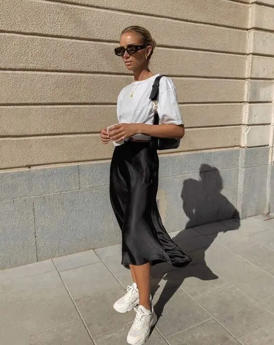 a casual look with a white t-shirt, a black slip midi skirt, white trainers and a black baguette bag