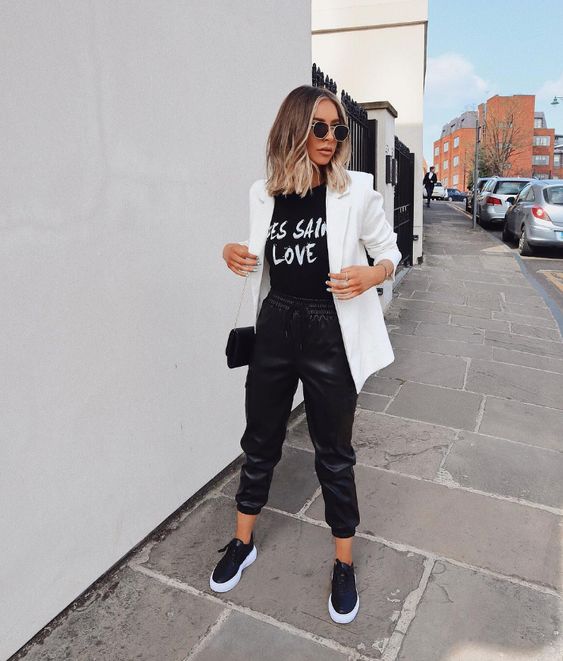 a casual monochromatic look with a printed black tee, black leather sporty pants, black platform shoe,s a white blazer and a black bag