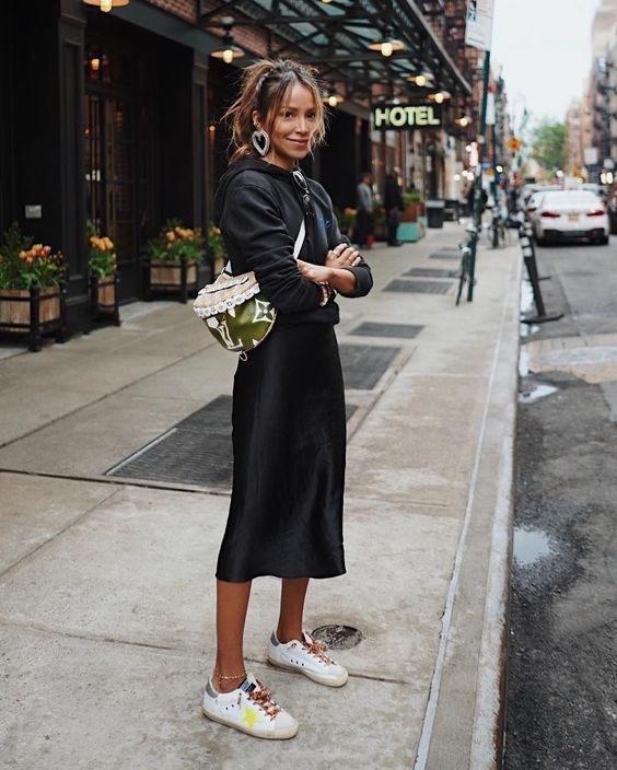 a catchy look with a black hoodie, a slip midi skirt, colorful sneakers and a bright bag