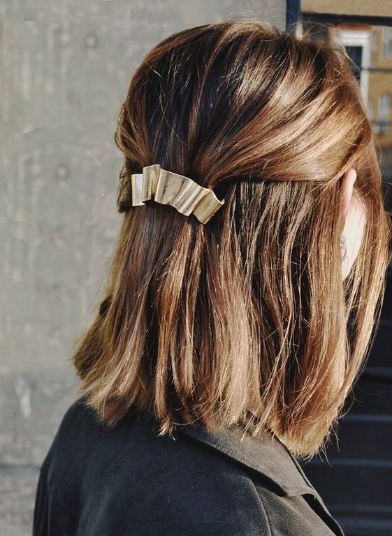 a classy half updo with a bump on top and straight hair down and a metallic hair barrette for a modern holiday party look