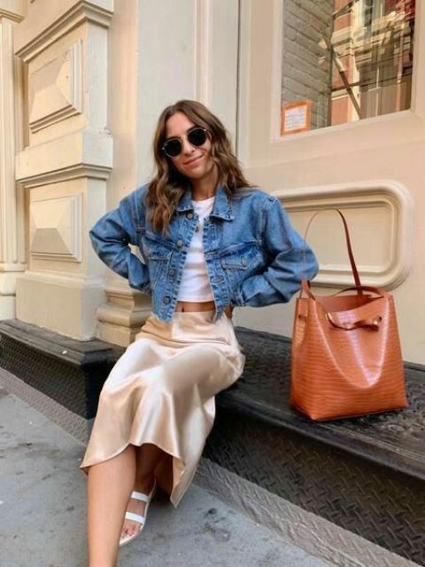 a classy spring look with a white crop top, a neutral satinmidi skirt, a blue cropped denim jacket, an amber bag and white shoes