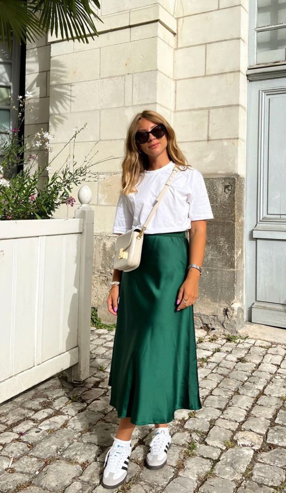 A classy spring look with a white t shirt, a green satin midi, white sneakers, a neutral bag is amazing