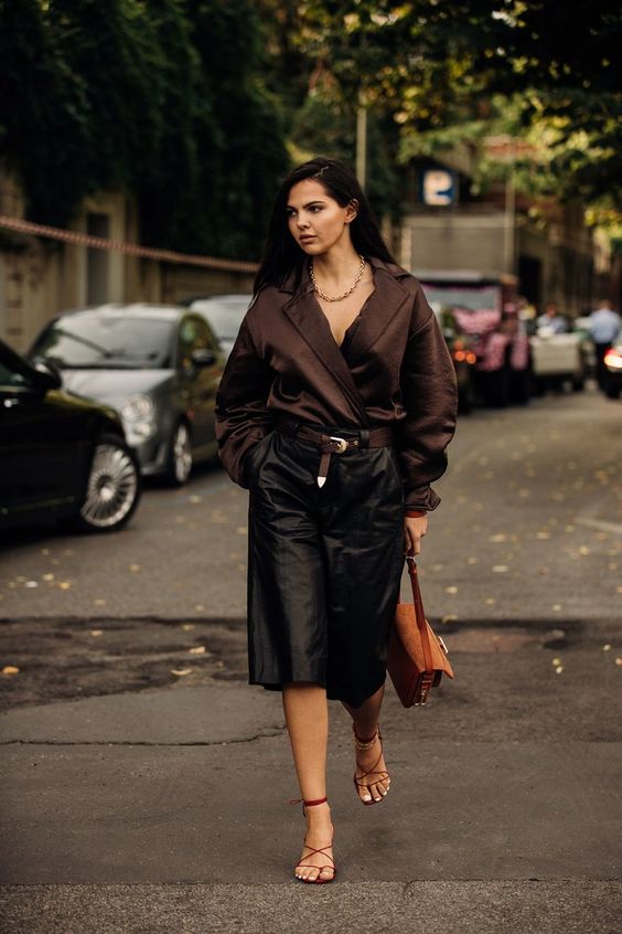 a luxurious outfit with a brown blouse, a statement necklace, black bermudas, brown lace up shoes and a brown bag