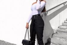 a monochromatic outfit with black cargo pants, a white off the shoulder top, white trainrs and a black bag