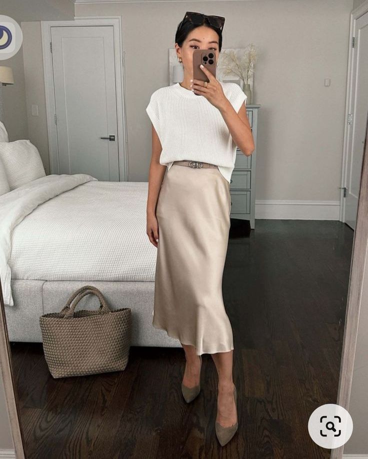 a spring work outfit with a sleeveless oversized top, a neutral satin midi skirt, taupe shoes and a woven tote