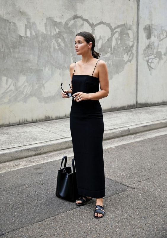 a black maxi fitting dress with thin straps, chic black slippers and a comfy black tote
