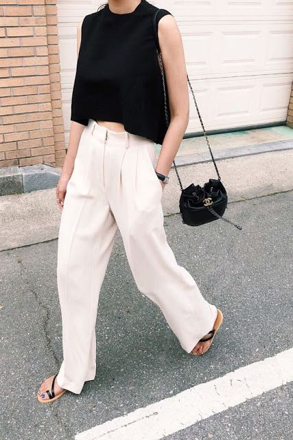 a minimalist outfit with an asymmetrical black crop top, white pants, a black bag and black Greek sandals