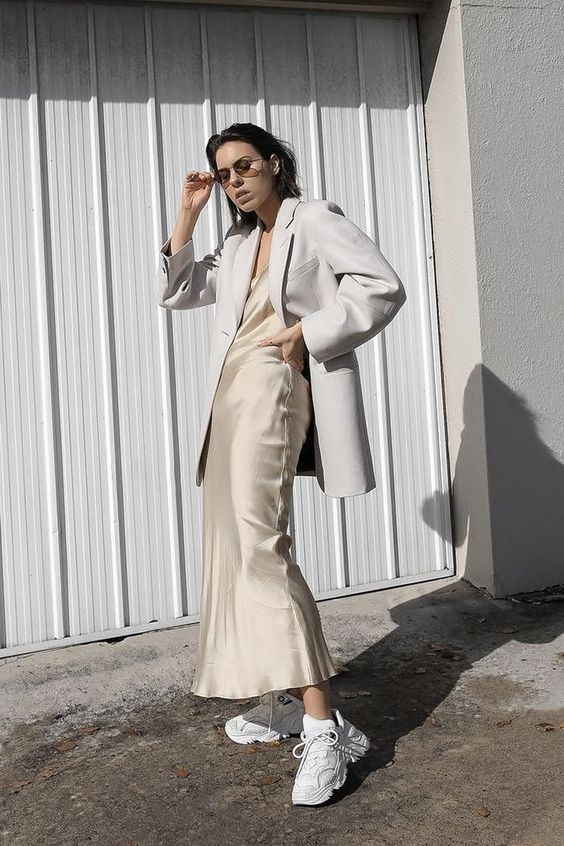 a neutral silk slip midi dress, a white oversized blazer and trainers for a trendy spring to summer look