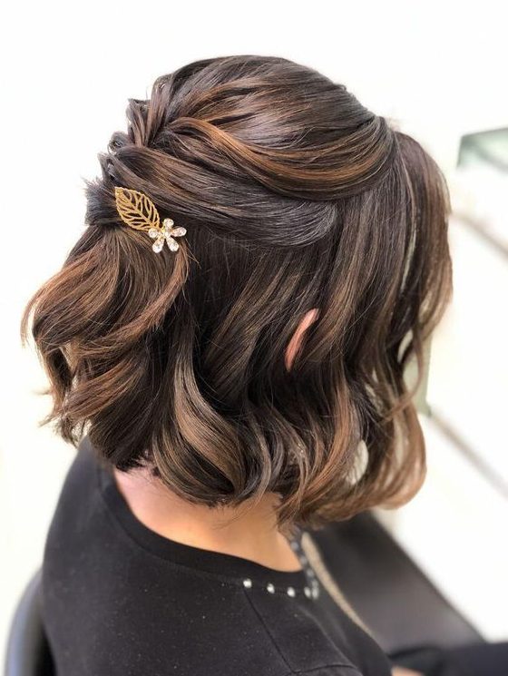 A refined half updo on medium length hair with twists and waves down, a little leaf and flower hair pin and face framing locks