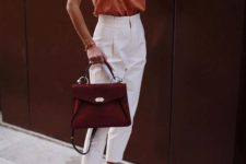 a rust-colored top, white high waisted pants, black sandals and a burgundy bag