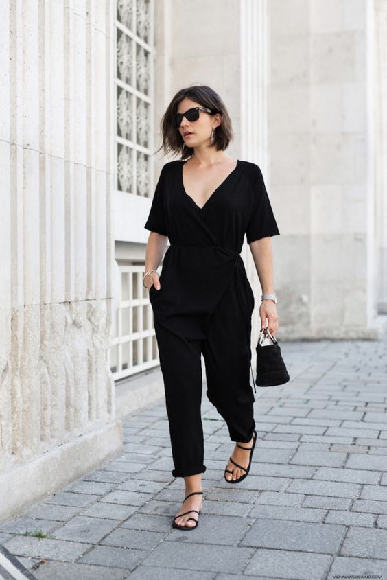 a summer party or work look with a black jumpsuit with a deep neckline, short sleeves, a black bucket bag and Greek sandals