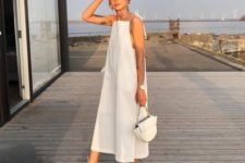 a white minimalist A-line midi dress with thin straps, open shoulders and sides, a catchy white bag and lace up shoes