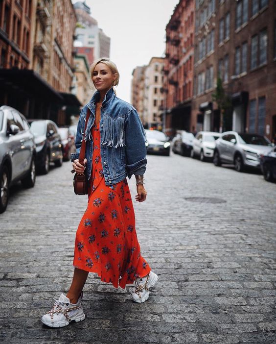 an orange floral print midi high low dress, an oversized denim jacket, statement trainers and a bag