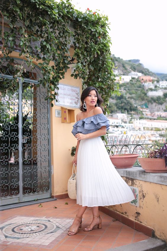 a blue ruffle off the shoulder top, a white pleated midi, nude block heels and a neutral bag