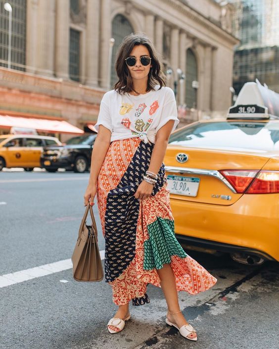 a bright printed t-shirt, a multi printed midi skirt, white slippers and a tan bag