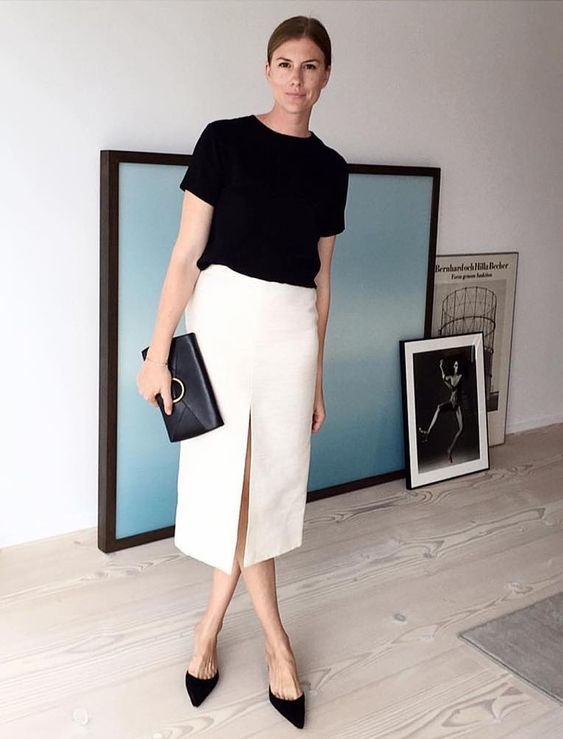 A minimalist look with a black t shirt, a white midi skirt with a front slit, black heeled mules and a black clutch