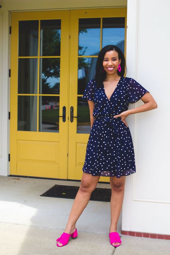 a navy polka dot knee dress, hot pink earrings and mules with block heels and tassels for a colorful touch